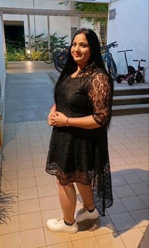 Woman in a black lace dress standing on a tiled floor with bicycles in the background.