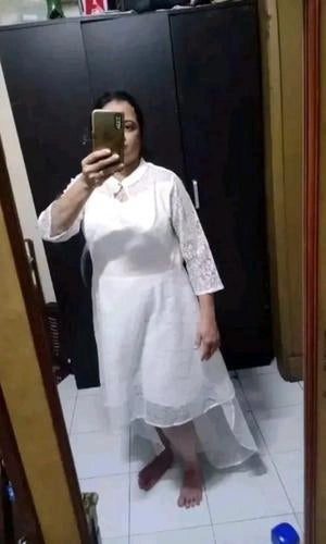 Person wearing a white dress standing in front of a black wardrobe.