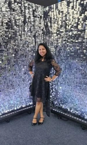 Woman in a black dress standing in front of a mirrored wall with a disco ball effect.