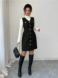 Woman wearing a black dress with white buttons, white turtleneck, and black knee-high boots in a minimalistic setting.