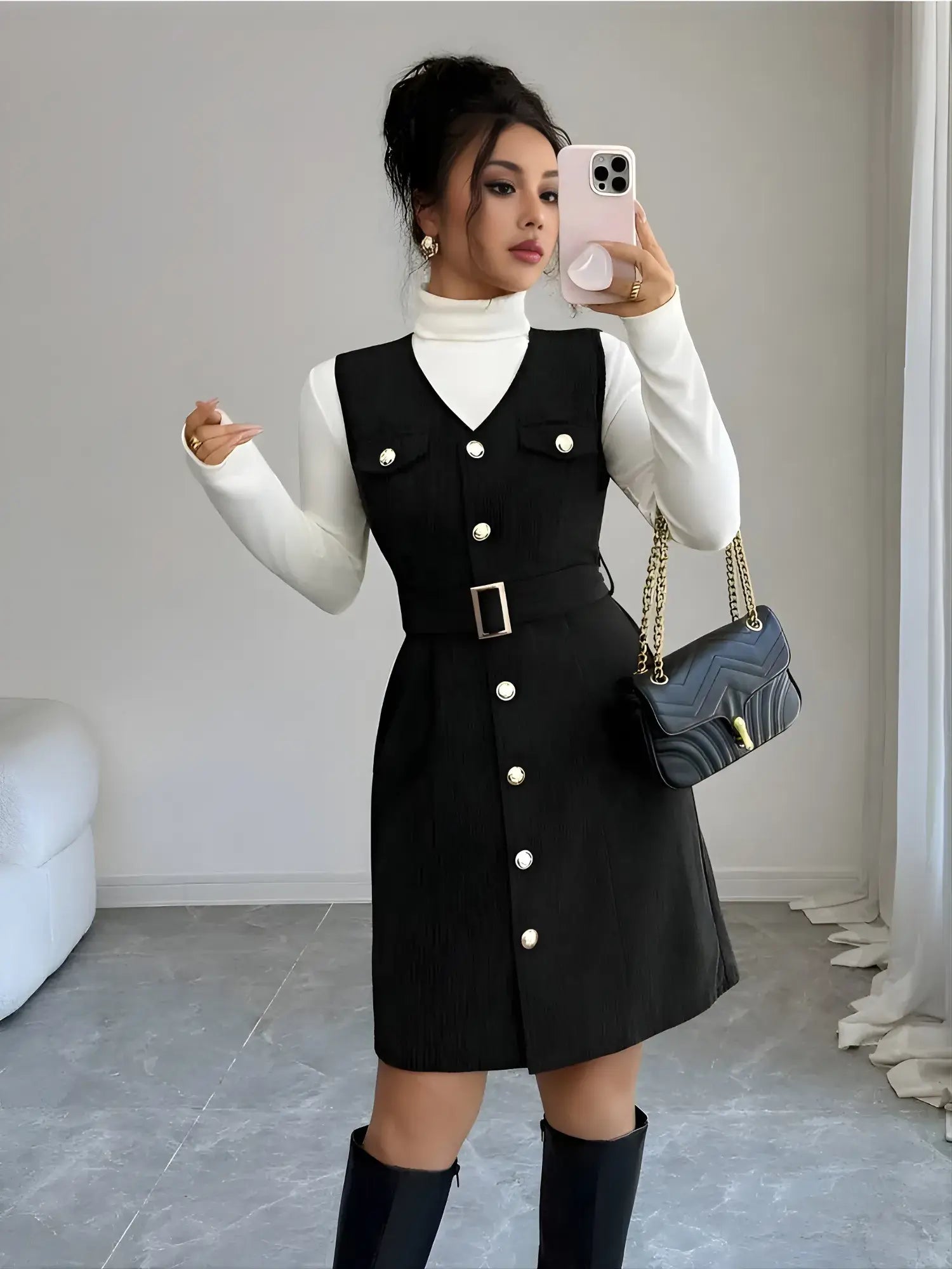Woman taking a mirror selfie wearing a black button-up dress with a white turtleneck and knee-high boots.