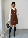 Woman wearing a brown dress with white buttons and black knee-high boots in a minimalistic setting.
