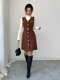 Woman wearing a brown dress with white buttons and black knee-high boots in a minimalistic setting.