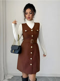 Woman wearing a brown dress with white buttons, holding a black handbag against a plain background
