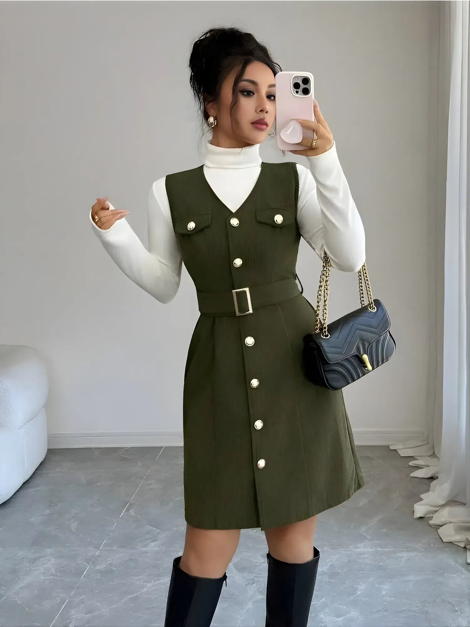 Woman taking a mirror selfie wearing a green dress with white buttons, white turtleneck, and black knee-high boots.