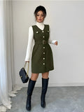 Woman wearing a green dress with white buttons and black knee-high boots, holding a black handbag.