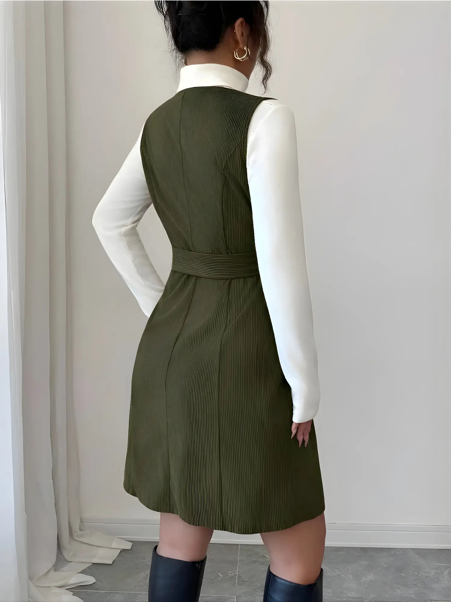 Person wearing a green dress over a white shirt against a plain background