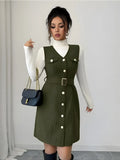 Woman wearing a green dress with white buttons, holding a blue handbag against a plain background
