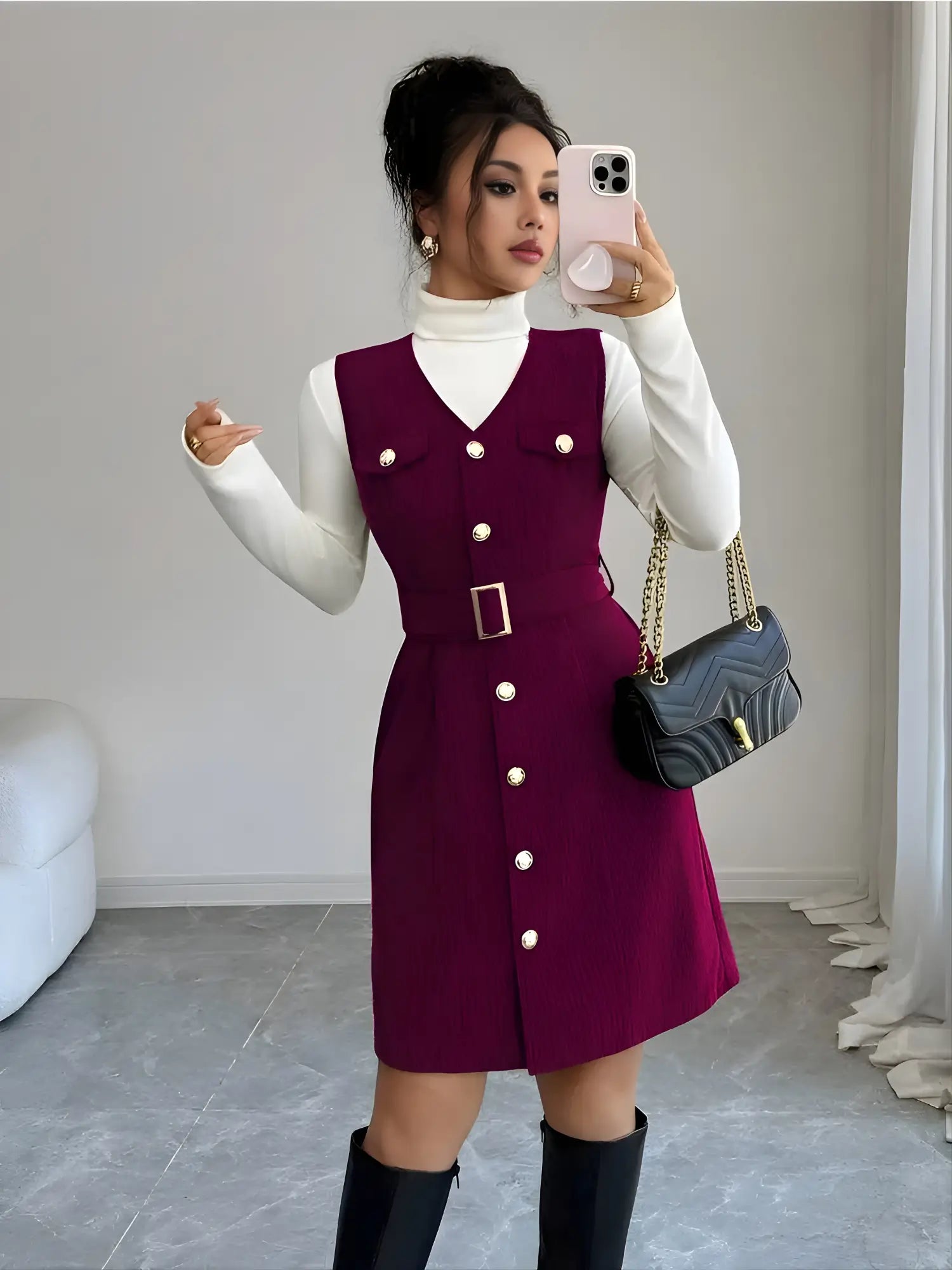 Woman taking a mirror selfie wearing a burgundy dress with white buttons, white turtleneck, black knee-high boots, and holding a black handbag.