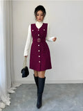 Woman wearing a purple dress with white buttons, white sweater, and black knee-high boots in a minimalistic setting.